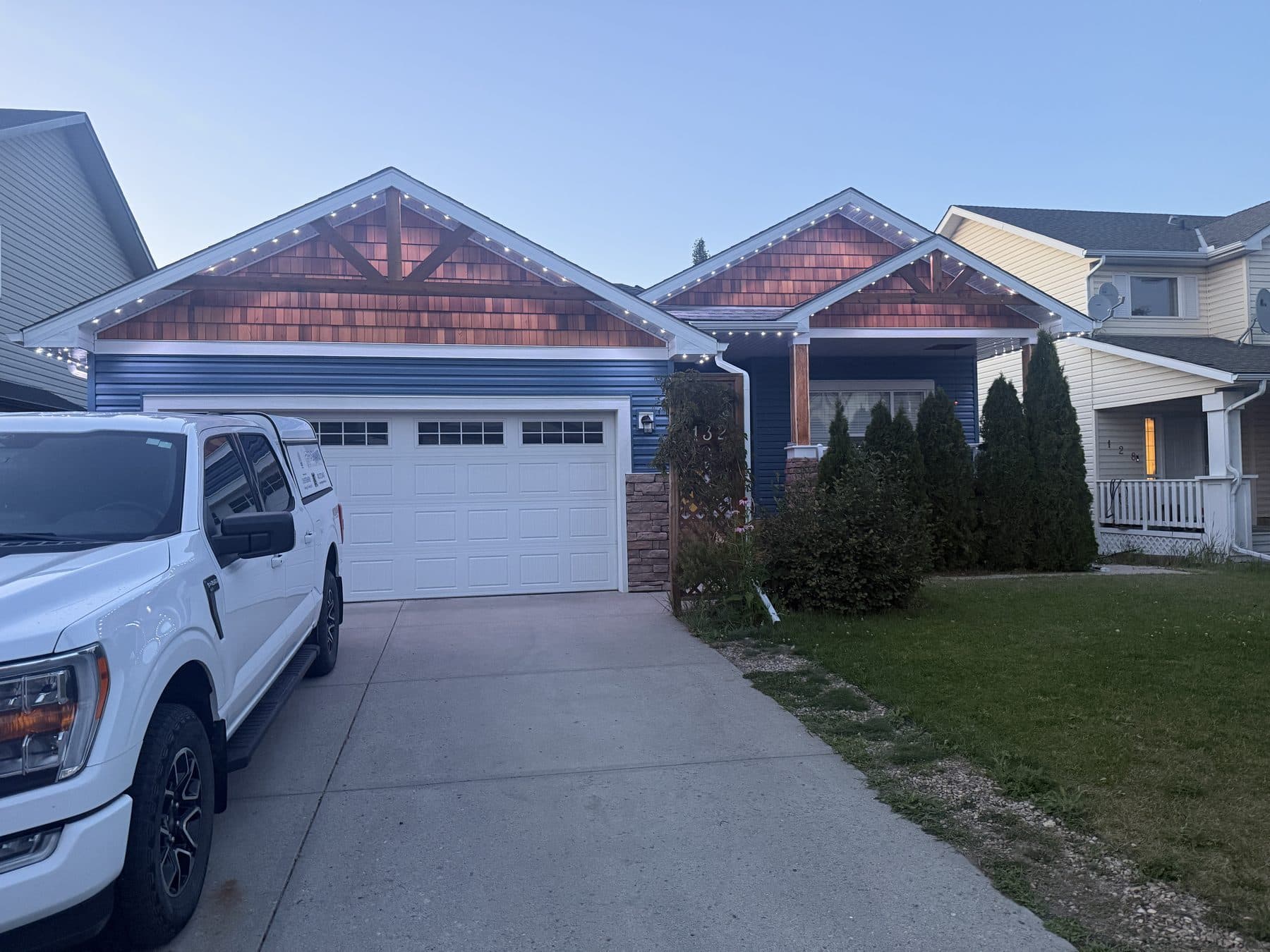 Permanent LED lights finished across all three gable peaks on a blue craftsman home at dusk