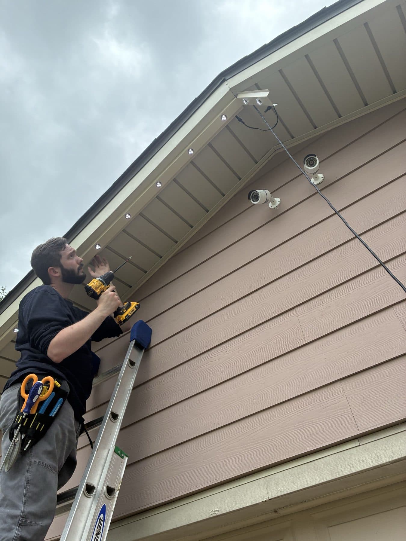 Installer on a ladder running permanent LED modules along a gable rake