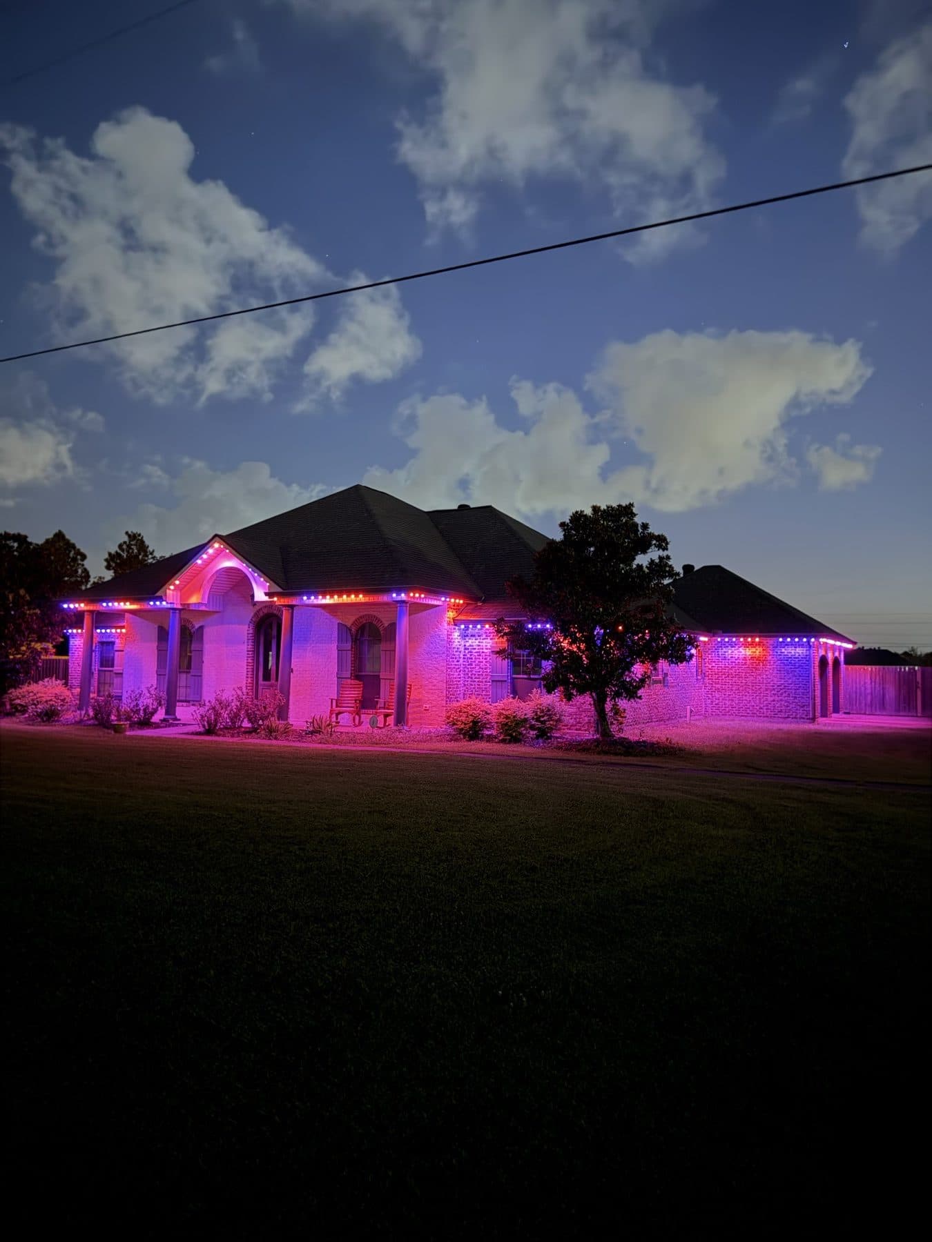 Red, white and blue permanent lighting scene on a brick home at dusk in Lake Charles