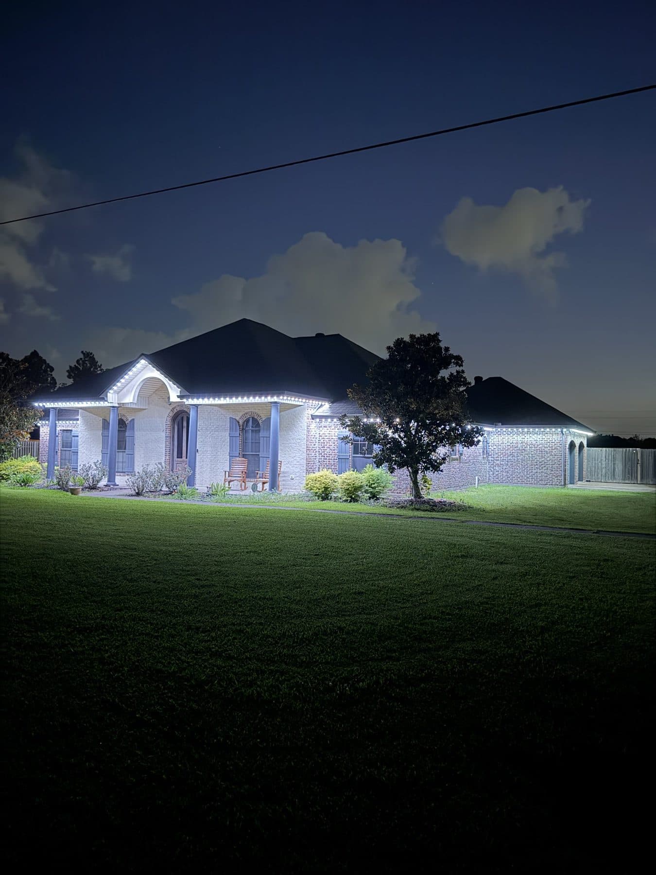 Warm white permanent lighting along the rooflines and porch of a brick home in Lake Charles