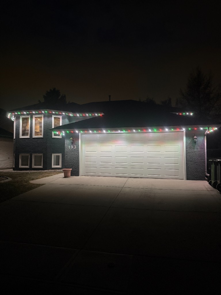 Chestermere home at night with red, green and white permanent lights along the roofline and garage